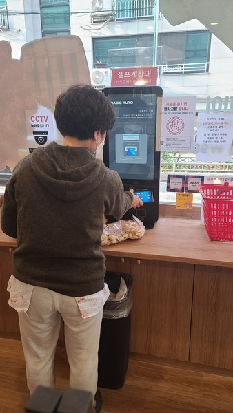 24시간 무인판매 시스템, 고객이 무인계산대에서 자율계산을 하고 있다.